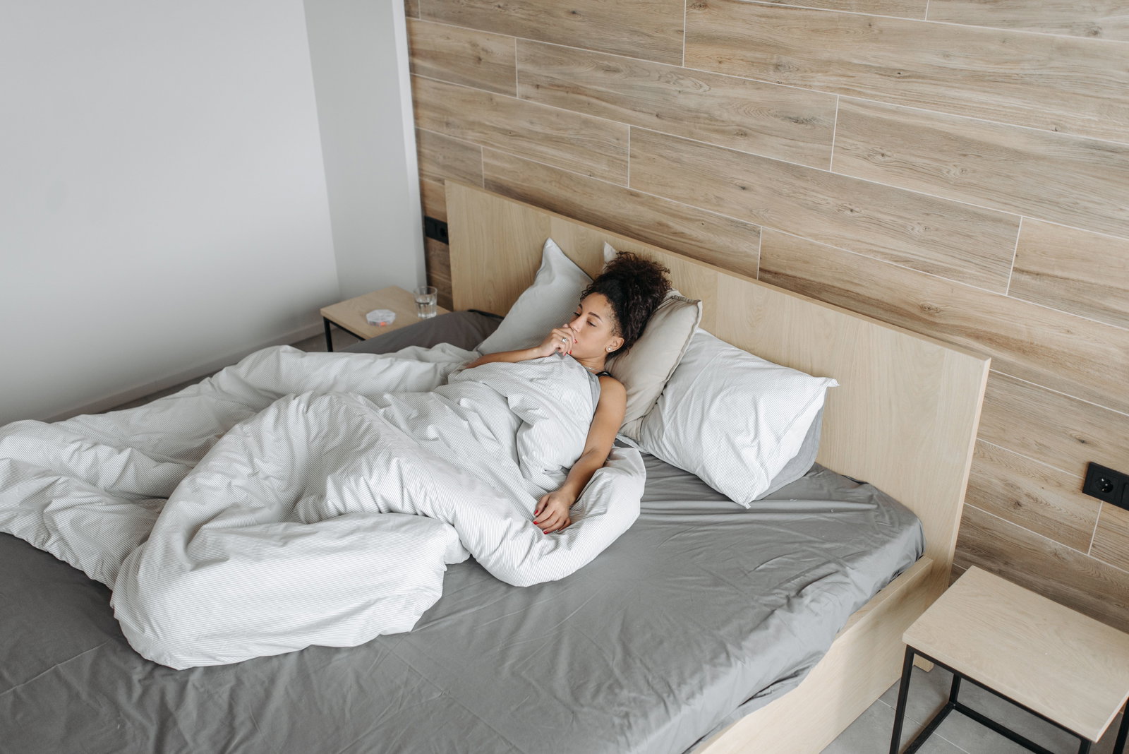 Frau liegt im Bett mit Decke und hustet, hat Hand vor dem Mund