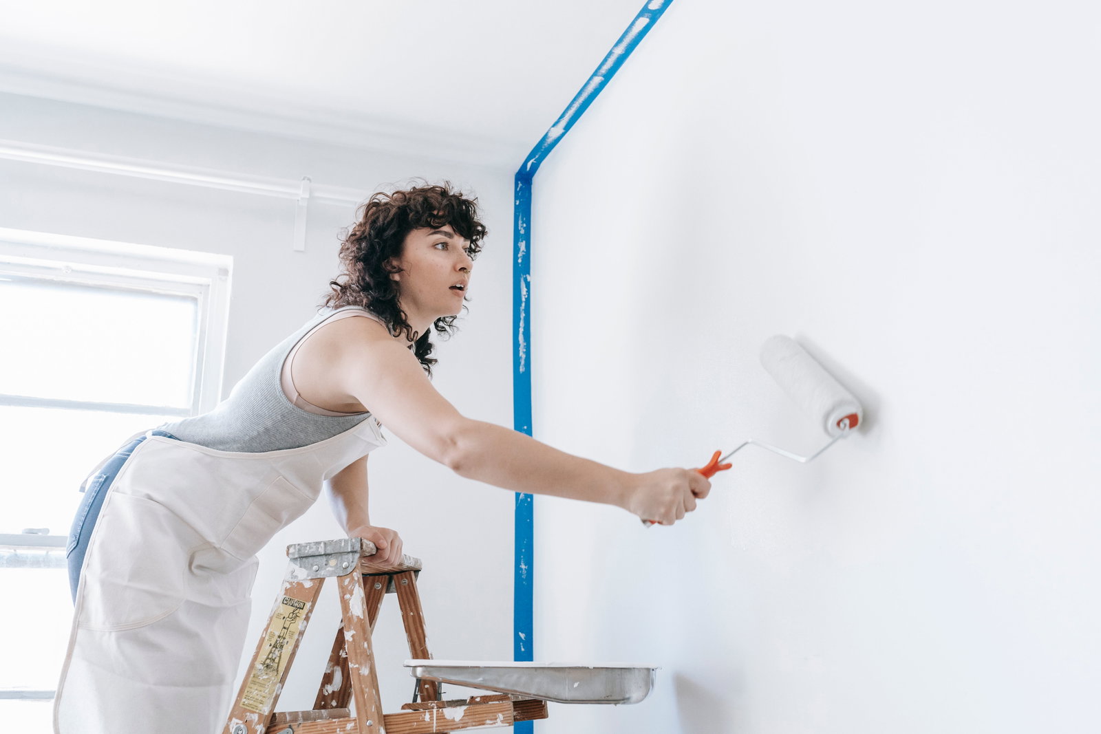 Malerin und Lackiererin streich mit einer Walze die Wand weiß