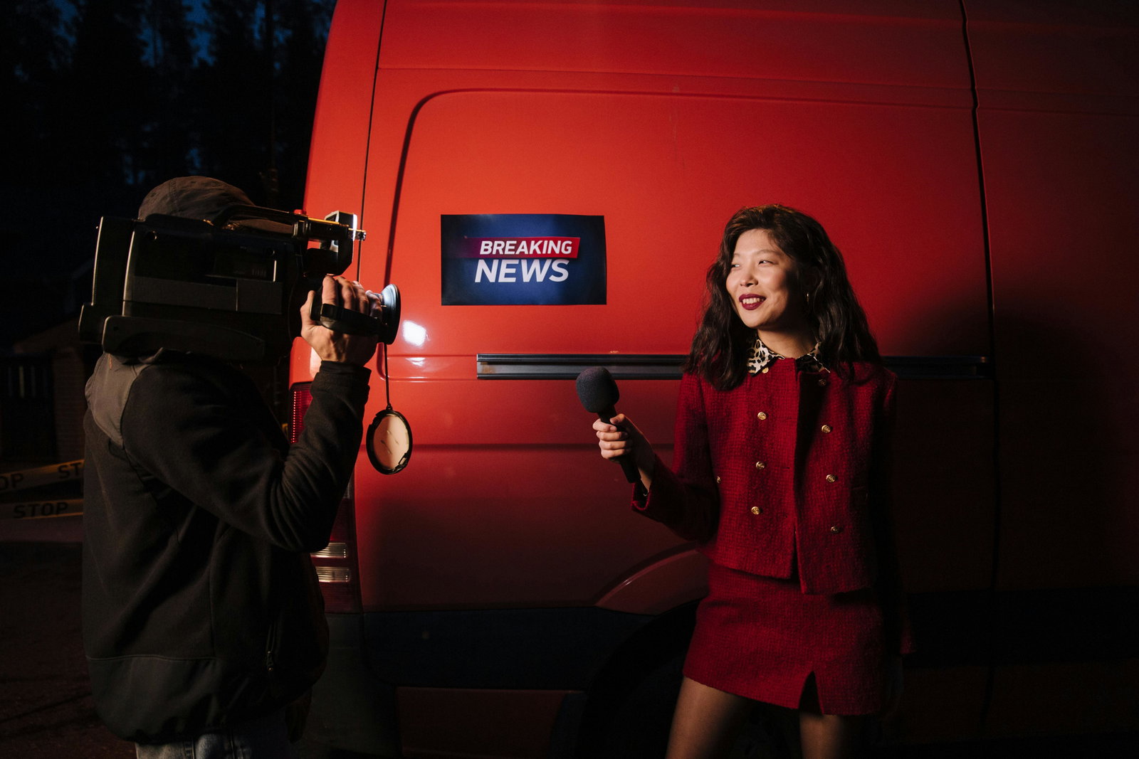 Journalistin steht mit Mikro vor einem roten Auto und wird gefilmt