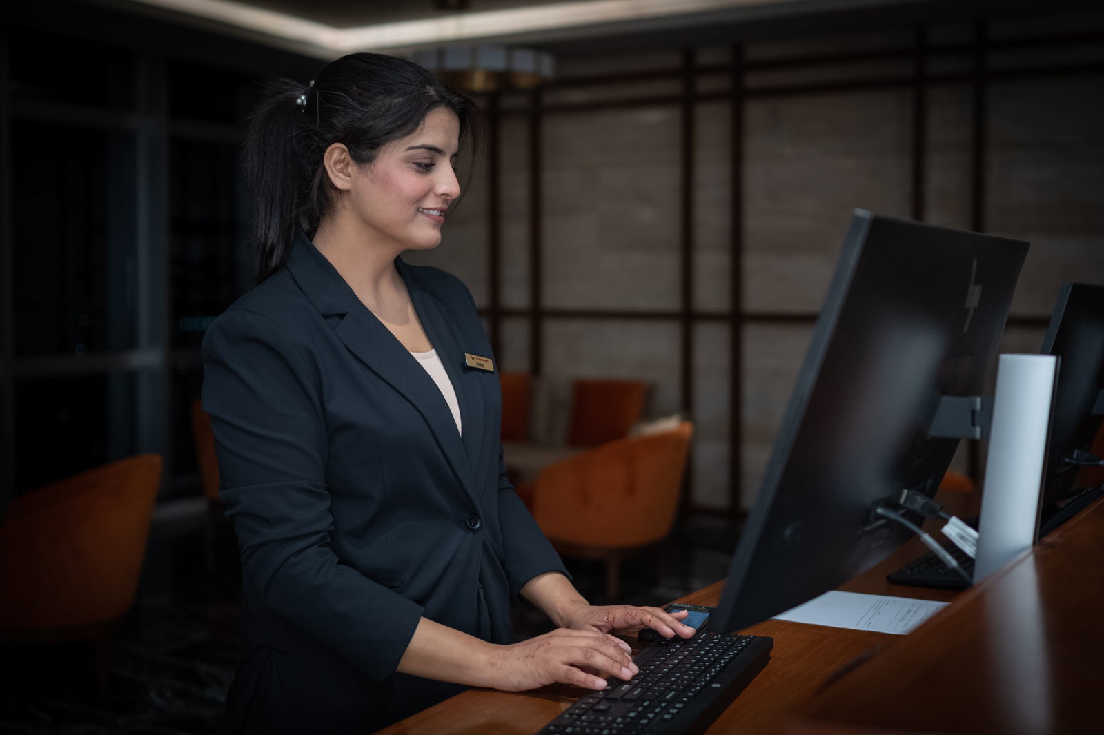 Hotelmanagerin steht an Rezeption und trägt Blazer 