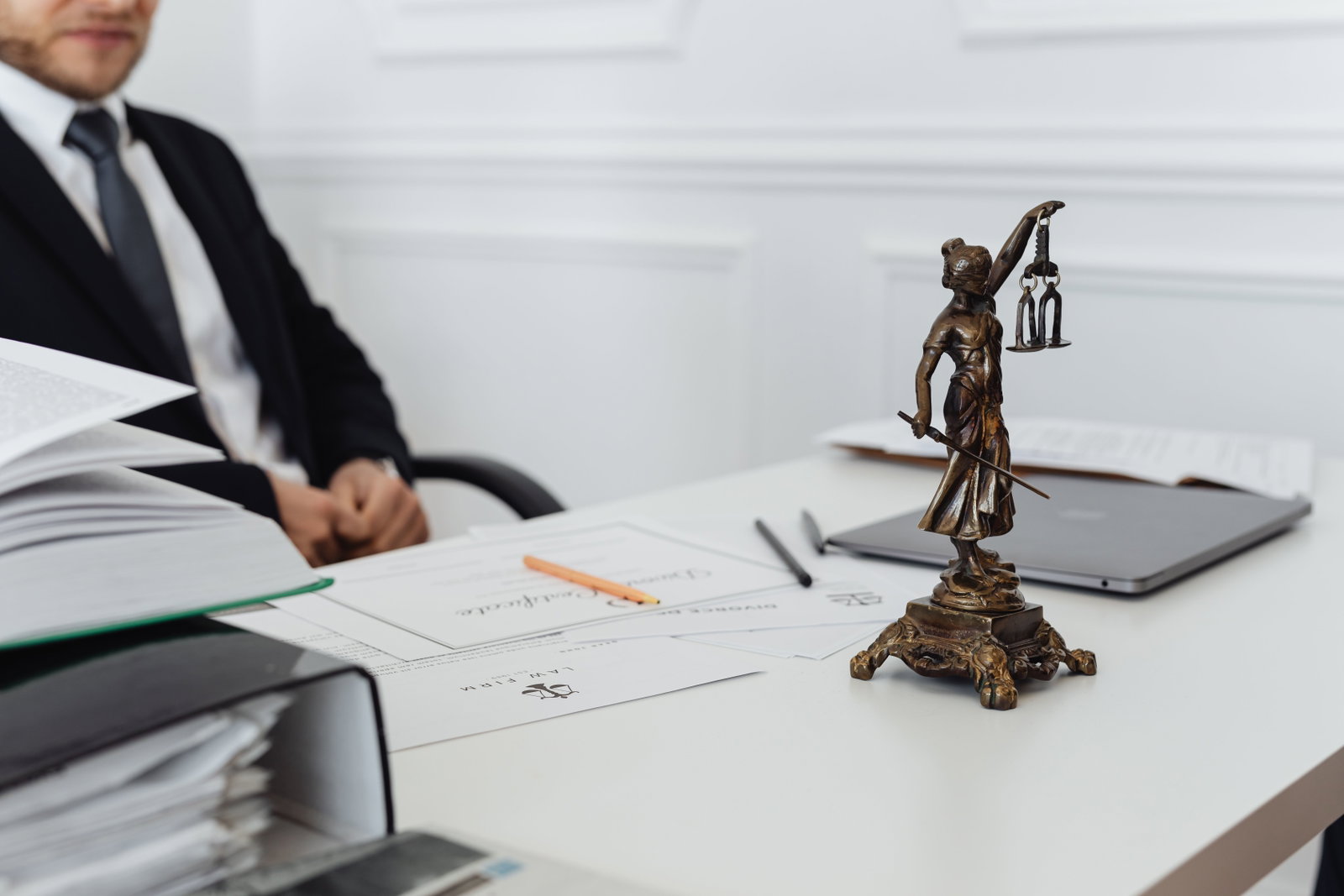 Mann im Anzug sitzt an einem Schreibtisch und schaut auf Akten, daneben Statue von einer Figur, wie im Gerichtssaal