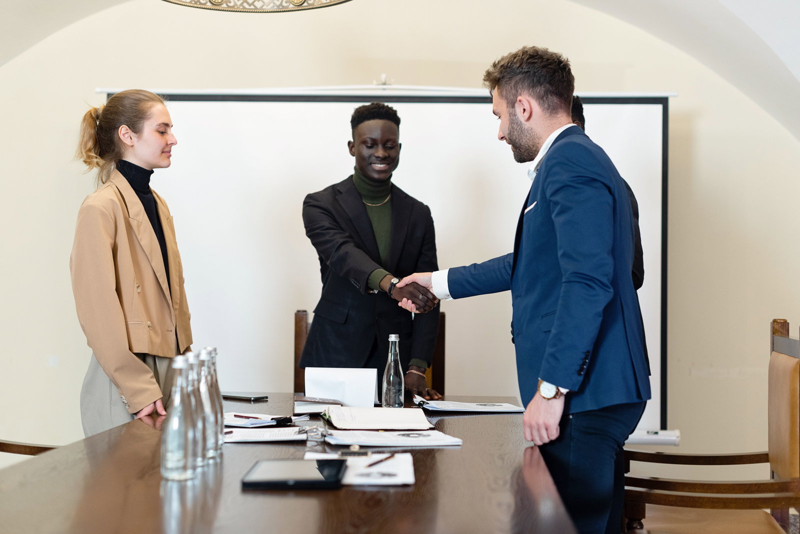 mehrere Personen in einem Raum geben sich die Hand in Anzug und Blazer