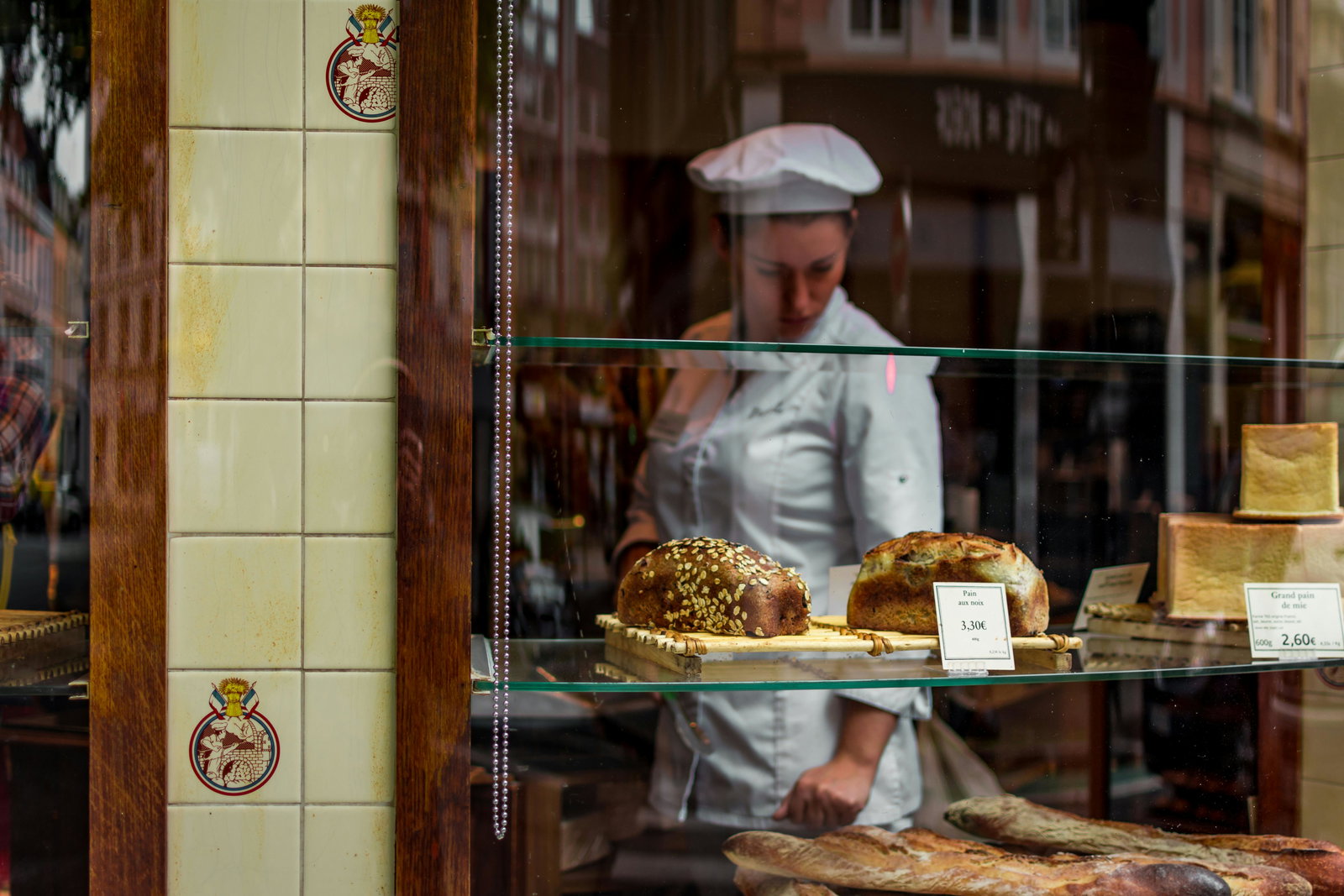Bäckerin steht in Schaufenster und schaut sich Backwahren an