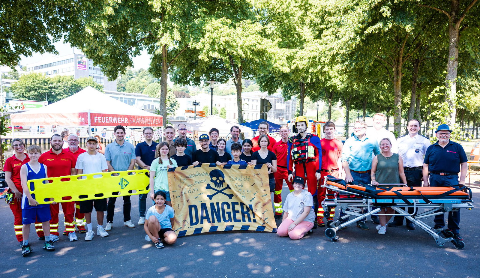 Zum Abschluss des Wasserrettungstags an der Saar versammeln sich Schülerinnen und Schüler der Klassenstufen 7 und 9 gemeinsam mit Vertretern von DLRG, Johannitern, Berufsfeuerwehr, Politik und weiteren Partnern zum Gruppenfoto.