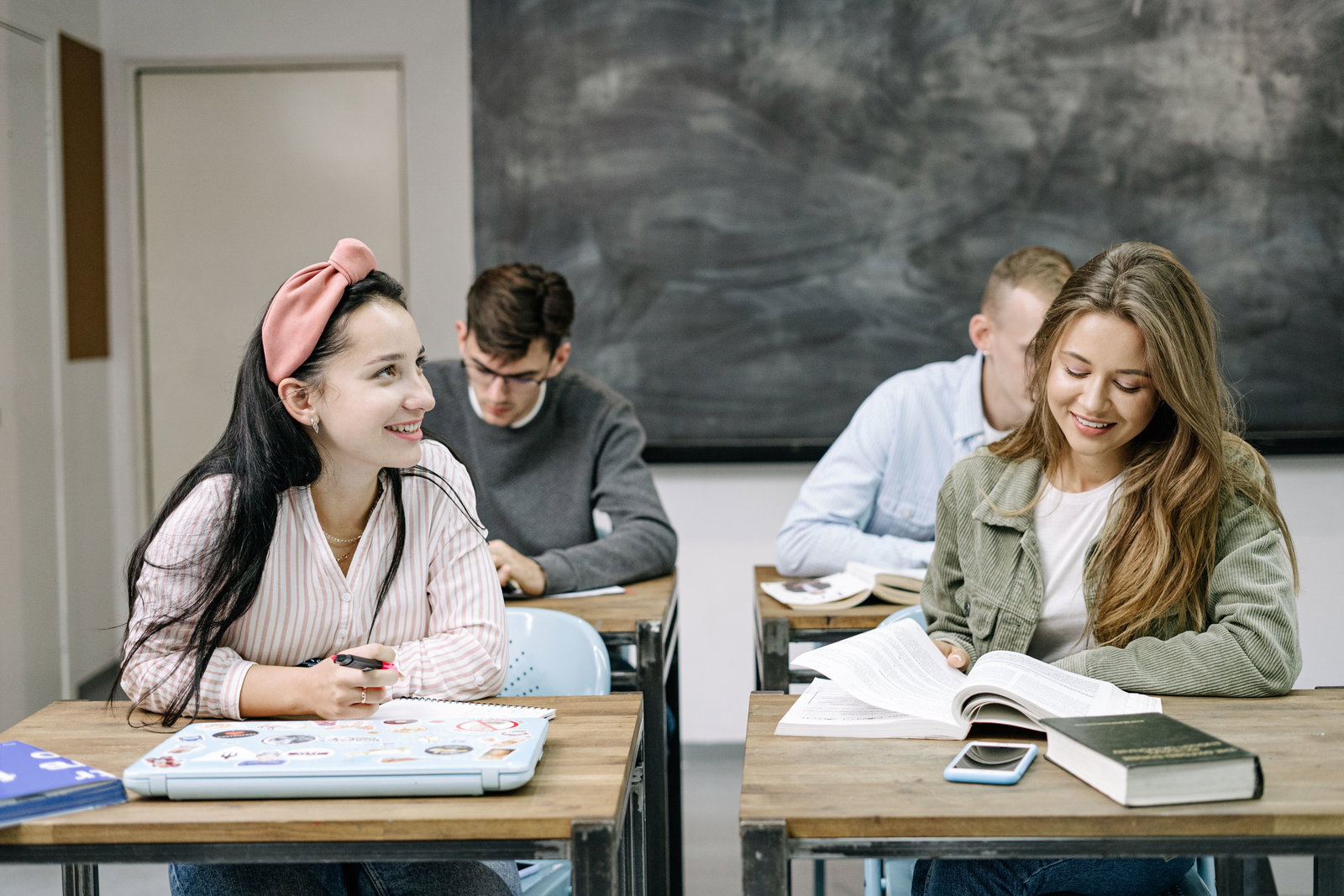 $ Studenten sitzen jeweils an ihrem Tisch, zwei Mädchen in der ersten Reihe und zwei Jungs dahinter, und lernen 