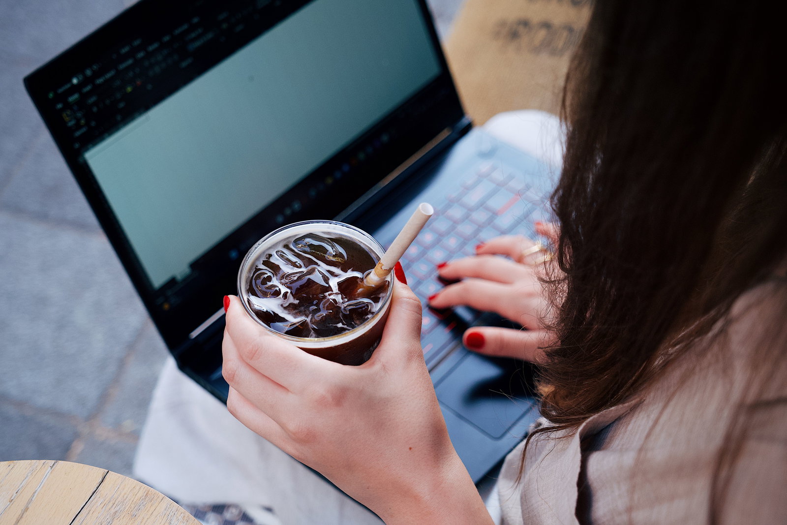 Mädchen mit Ice-Kaffee in der Hand und schreibt am Laptop