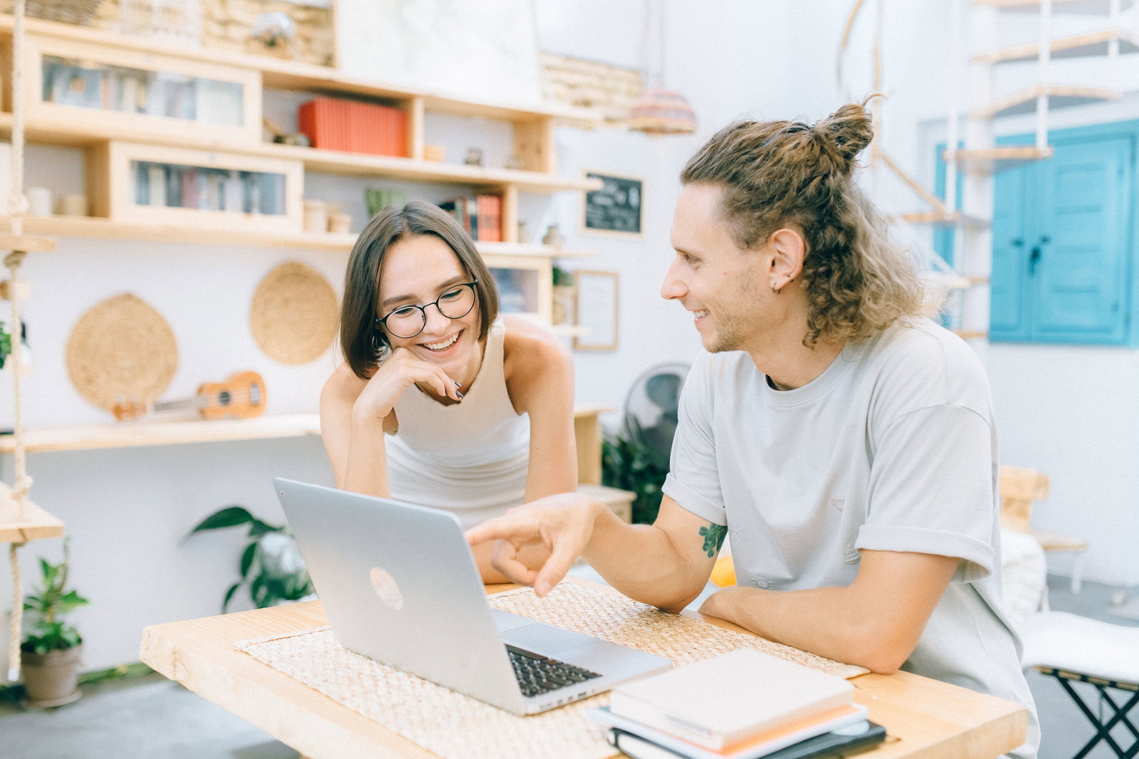 Zwei junge Menschen sitzen vor einem Laptop und reden und sitzen an einem Tisch