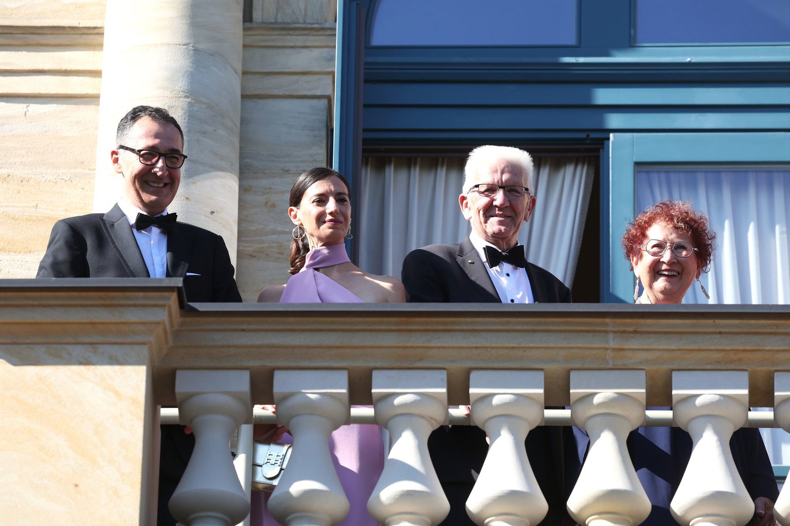 Auf dem Balkon des Festspielhauses warten Cem Özdemir, Flavia Zaka, Winfried Kretschmann und Gerlinde Kretschmann auf den Beginn des Festakts.