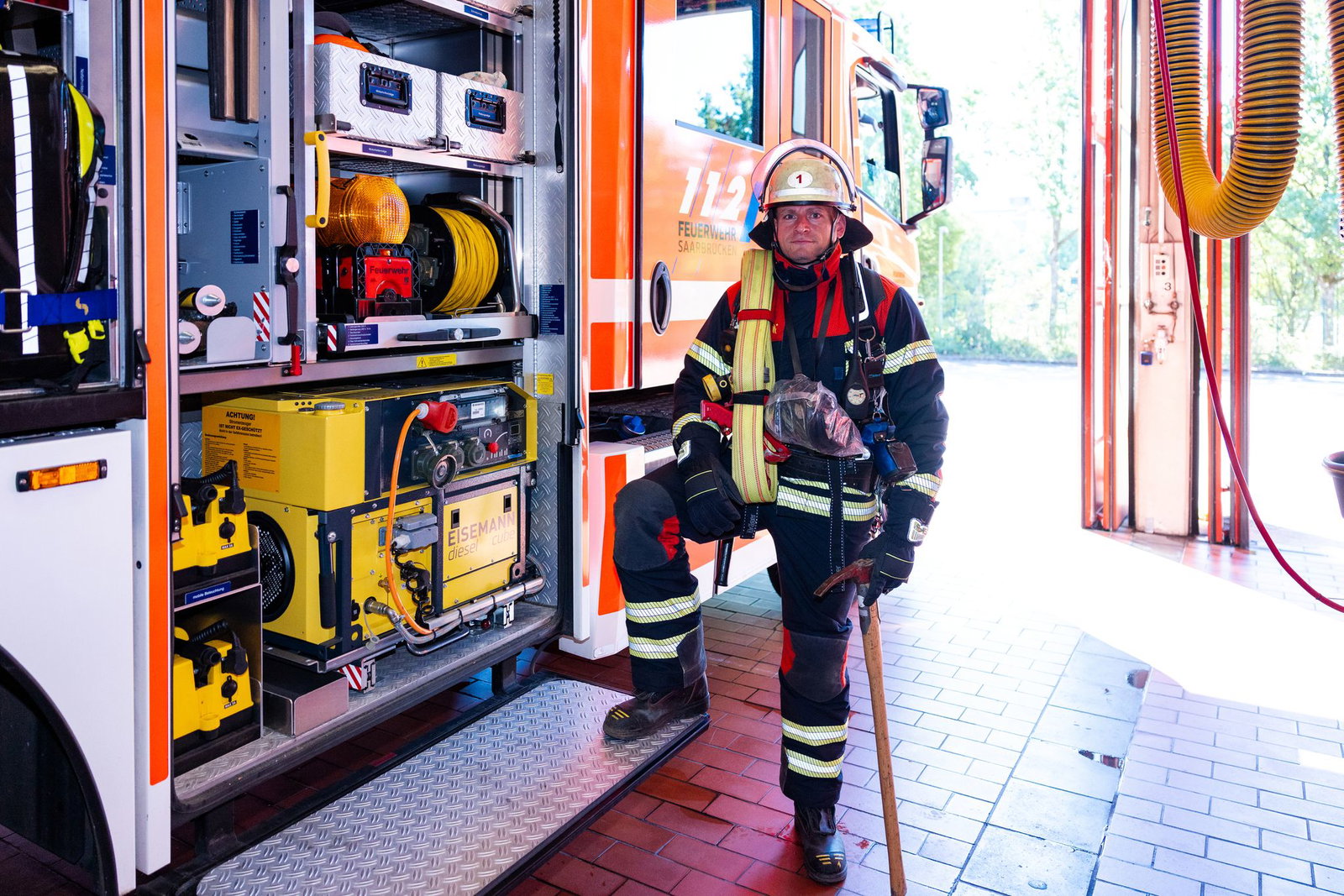 Hauptbrandmeister Kevin Michel steht in voller Schutzausrüstung neben einem Löschfahrzeug der Berufsfeuerwehr Saarbrücken.