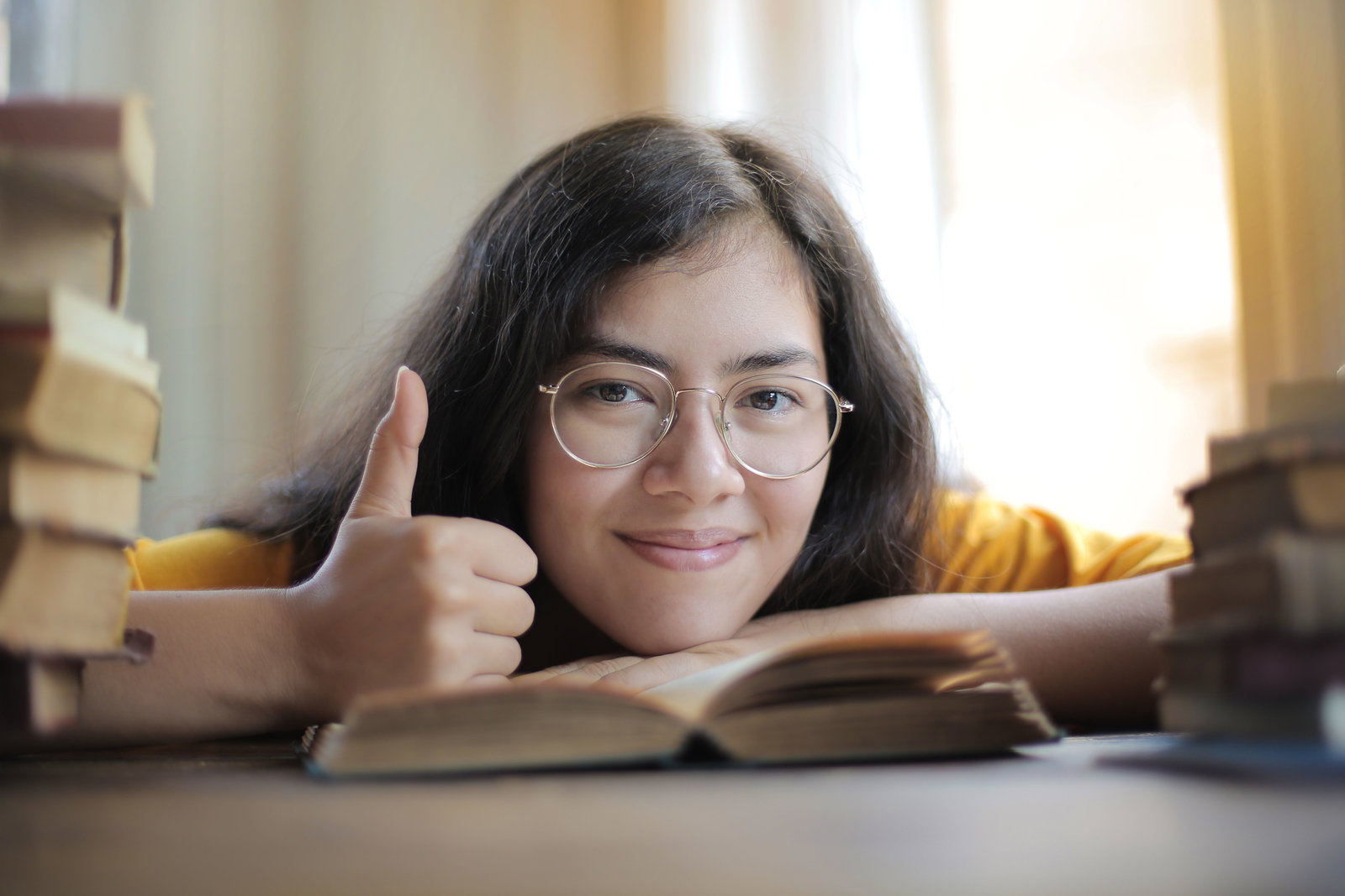 Frau liegt auf Schreibtisch, auf einem Buch und zeigt Daumen hoch