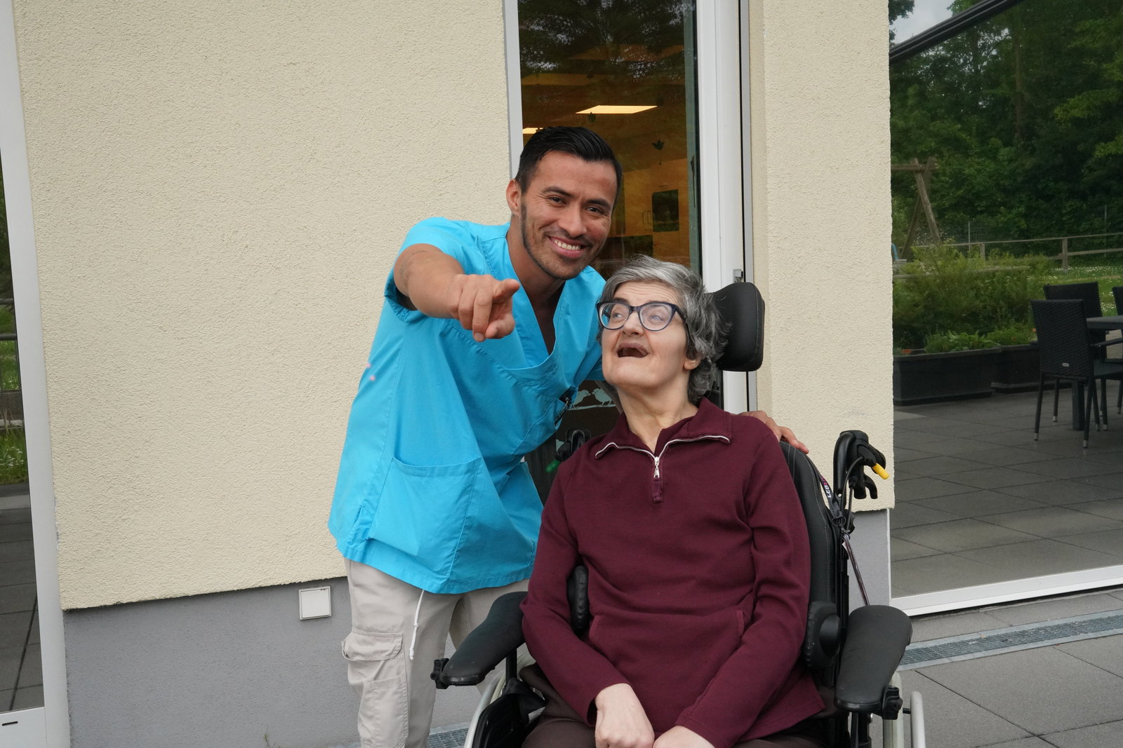 Lebenshilfe Mann zeigt auf Kamera Frau im Rollstuhl lacht