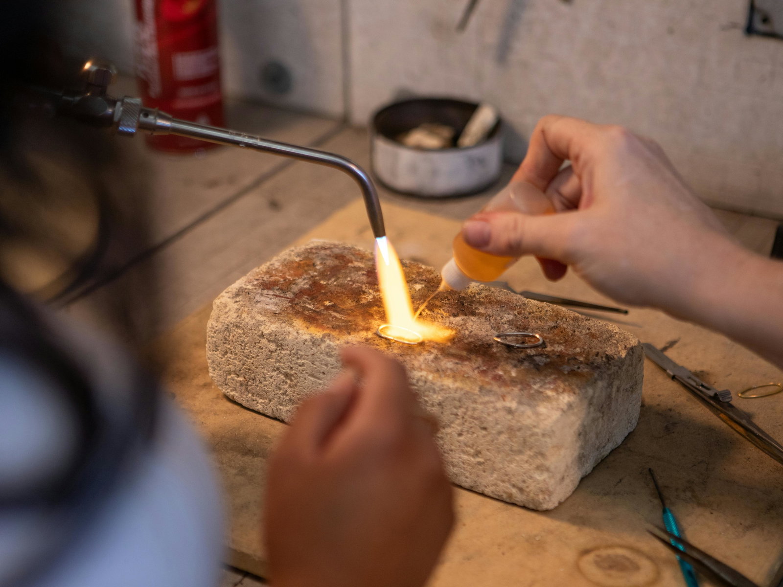 Goldschmiedin hält Flamme auf Ring und spritzt Flüssigkeit auf einem Fläschchen drauf