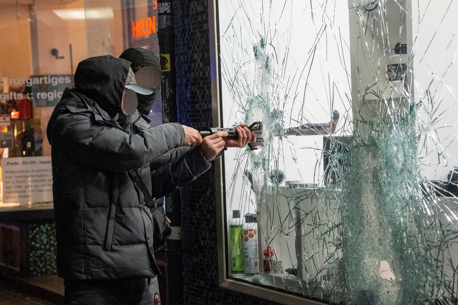 Zwei Männer stehlen durch die eingeschlagene Scheibe eines Waffengeschäft eine Waffe. 