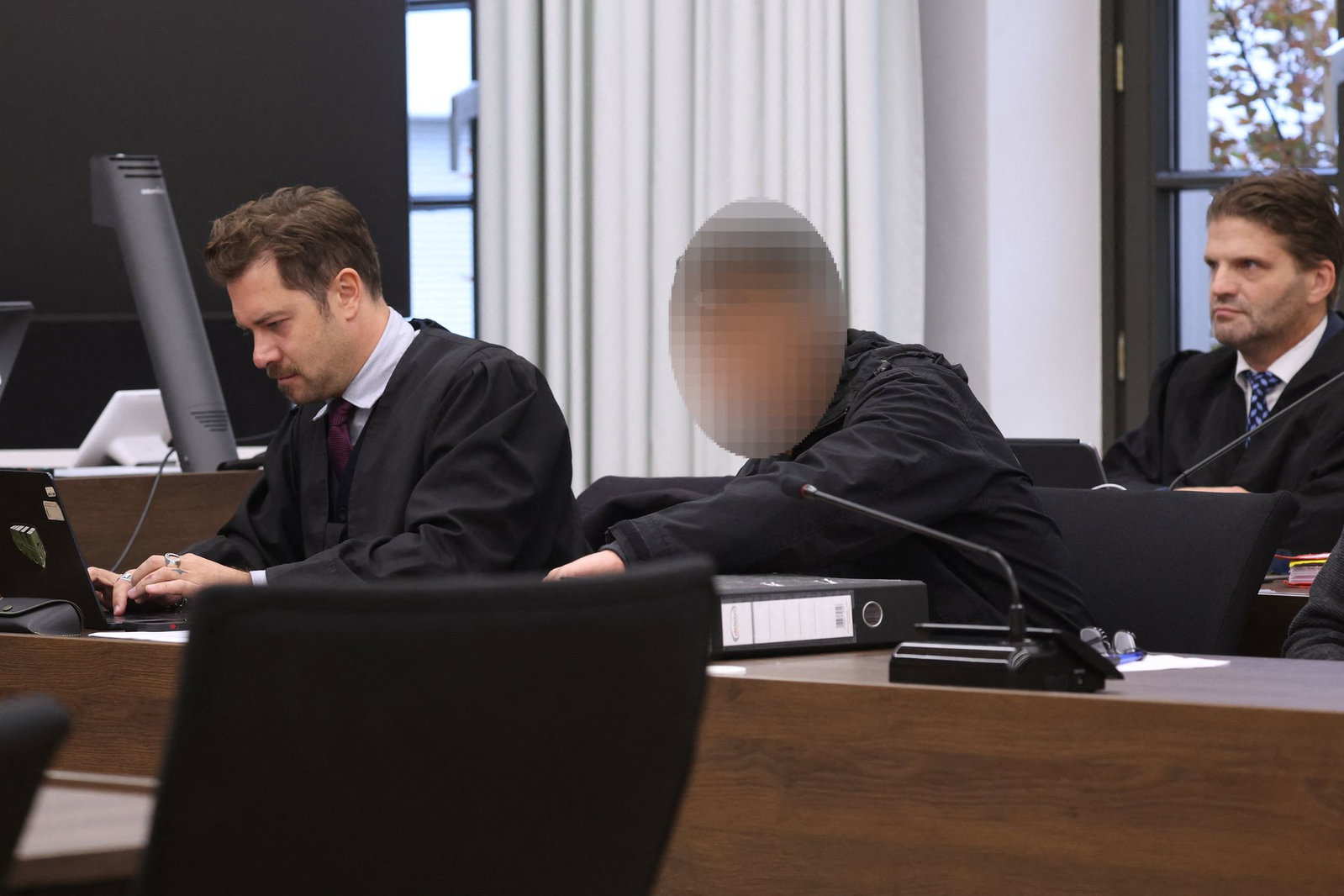 Der Angeklagte sitzt zwischen seinen beiden Rechtsanwälten im Gerichtssaal.