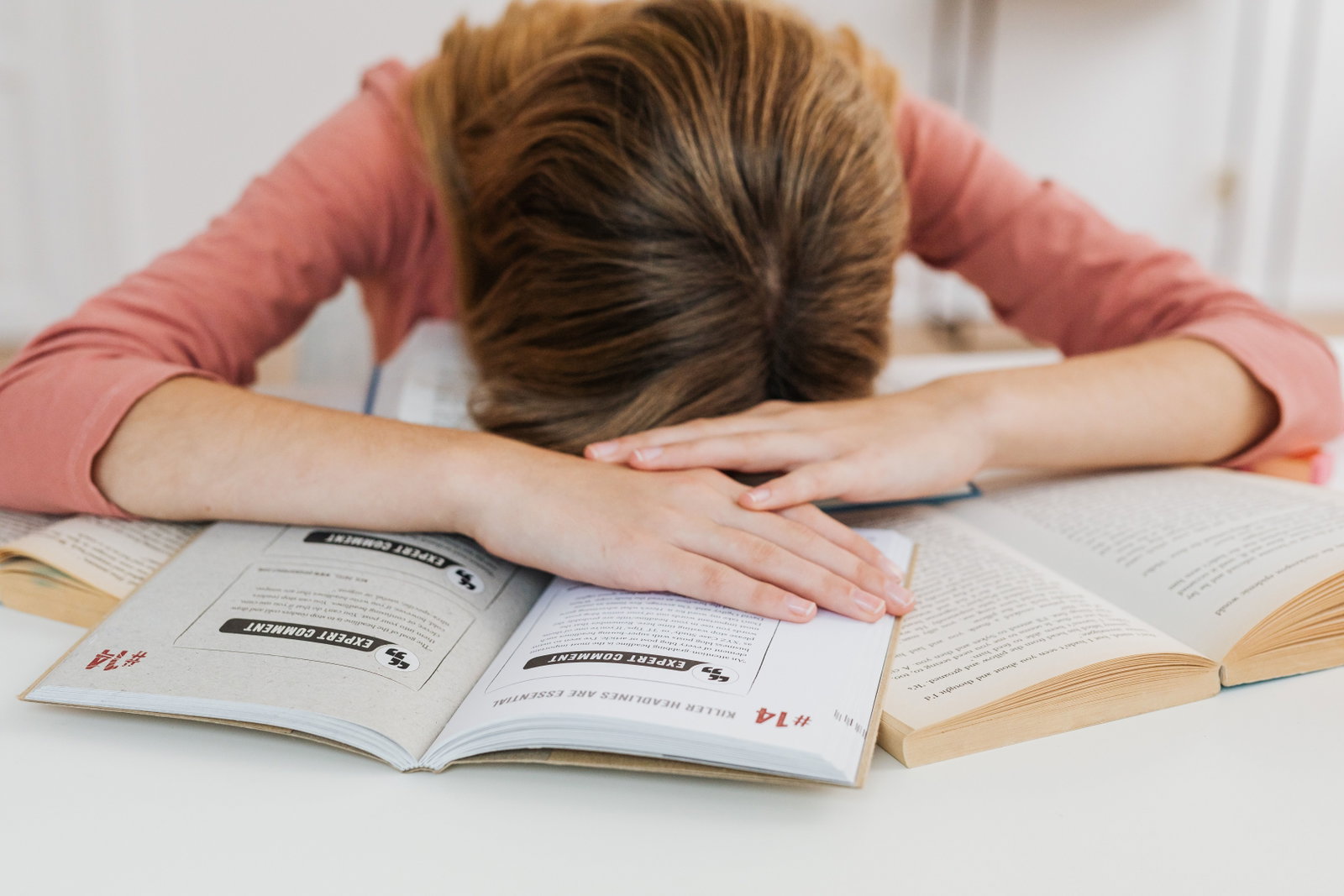 Eine von den Studien überwältigte Schülerin schläft über offenen Büchern an einem Schreibtisch ein, was die akademische Ermüdung darstellt.