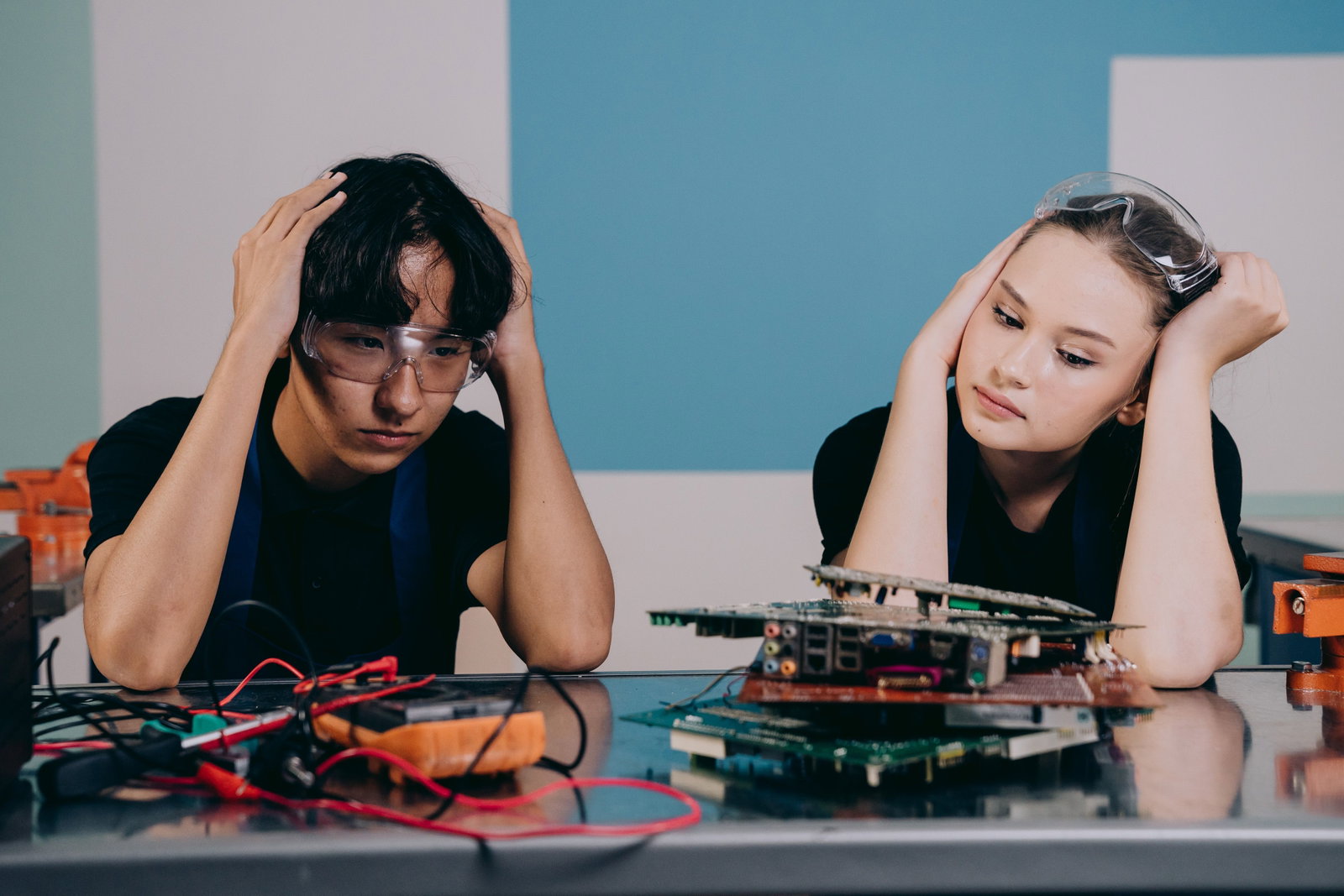 Zwei Techniker in Schutzbrillen arbeiten an Leiterplatten und zeigen Stress und Konzentration in einem Techniklabor.
