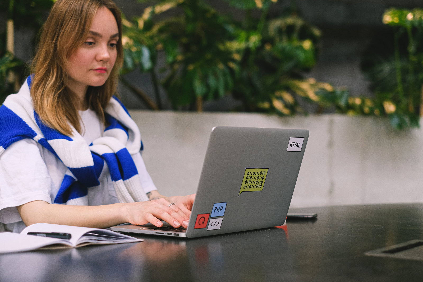 Frau mit gestreiftem Pulli siezt an Tisch und schaut in Laptop 