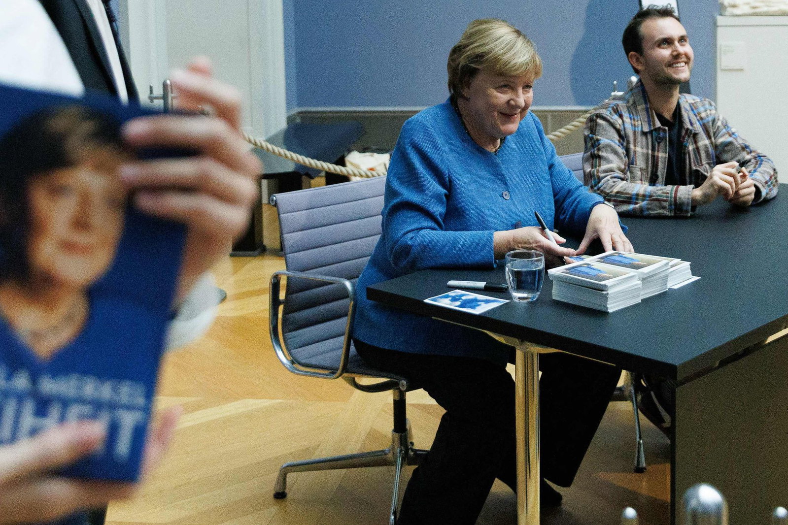 Merkel signiert Kunstpostkarten im Bode-Museum neben dem Maler ihres dort ausgestellten Porträts, Jérémie Queyras. 
